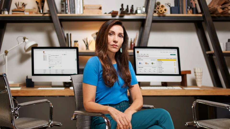 businesswoman sitting in a chair in front of two computers with UPS applications on the screens