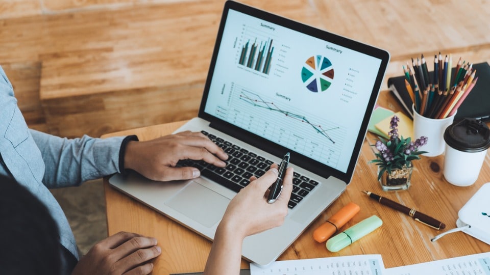 Two business professionals viewing graphs on a laptop and on printed paper