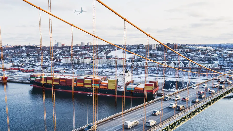 Rush hour traffic on a bridge above a container ship docked at pier 