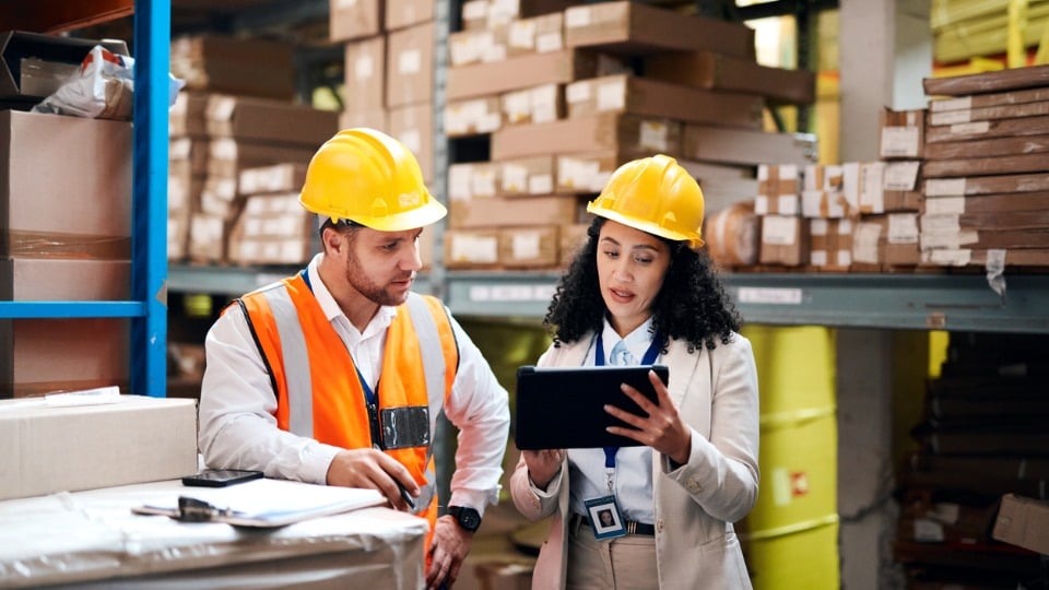 Two businesspeople in a warehouse reading a tablet