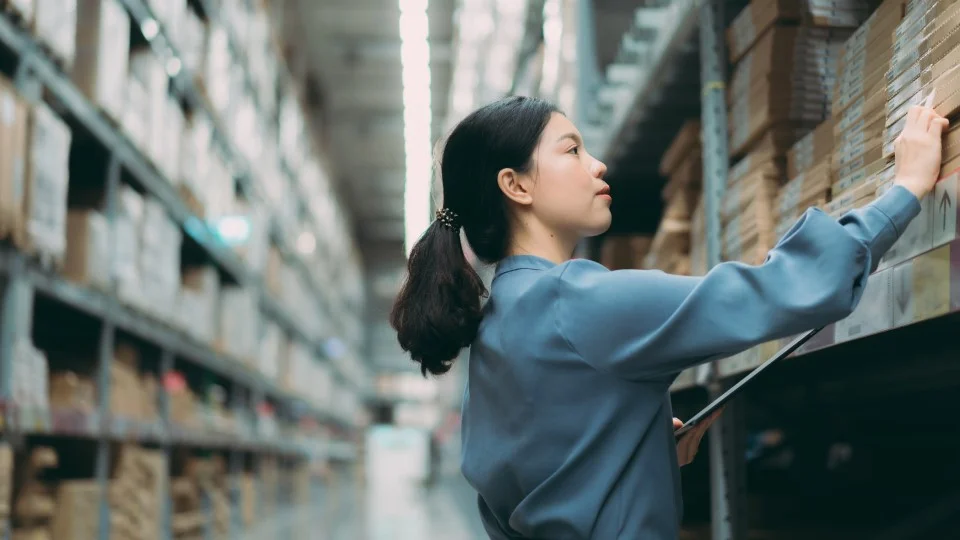 Asian businesswoman using a digital tablet to checking products on a shelf bay in a warehouse