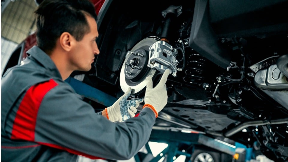 Car mechanic working on a lifted automobile at auto repair garage shop