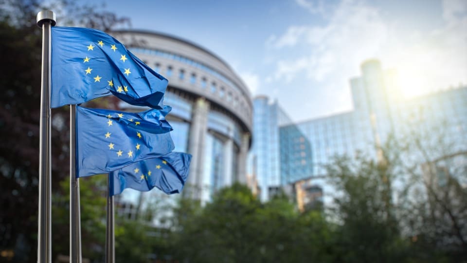 Three European Union flags waving outside of a building