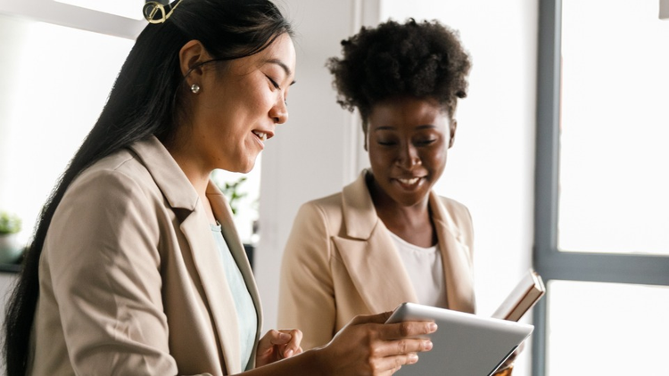 two professional women reading something on a tablet device